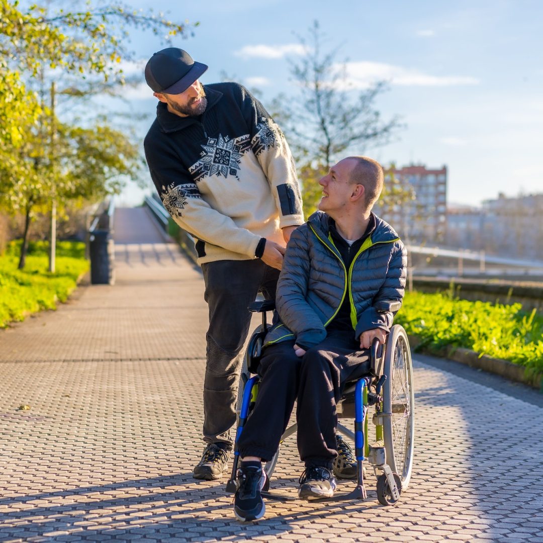Disabled person in wheelchair with friend overjoyed, smiling, enjoying with arms up